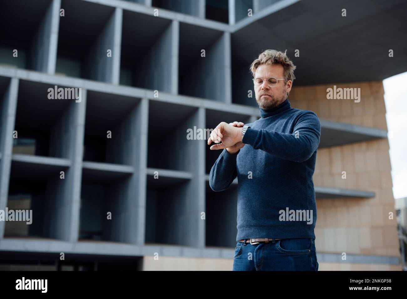 Ein Geschäftsmann, der die Zeit auf der Armbanduhr vor dem Gebäude überprüft Stockfoto