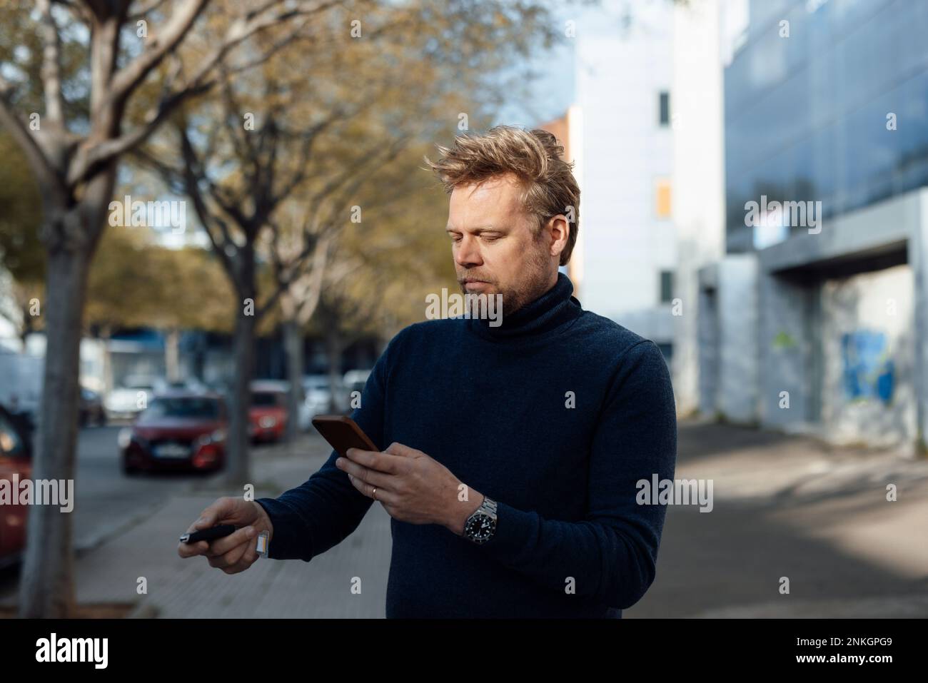 Mann, der mit Schlüssel verriegelt und ein Smartphone benutzt Stockfoto