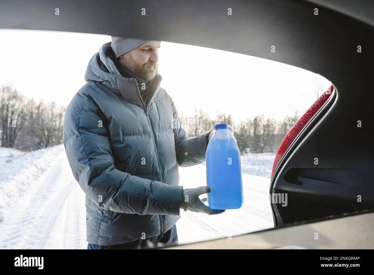 Ein Mann, der im Winter eine Flasche Auto-Frostschutzmittel aus dem Kofferraum nimmt Stockfoto