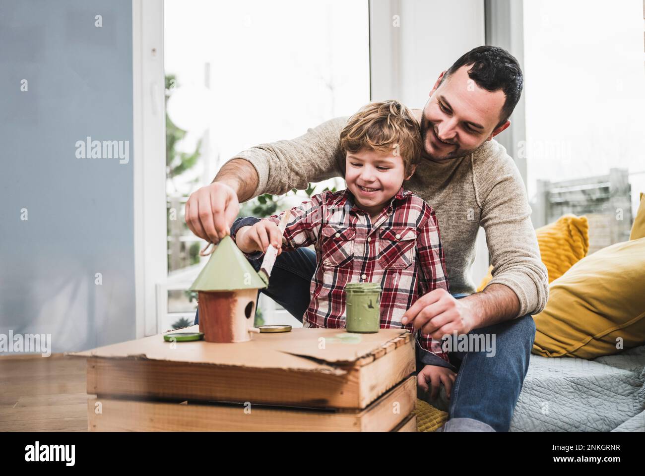 Glücklicher Vater und Sohn, der zu Hause ein Modellhaus malt Stockfoto