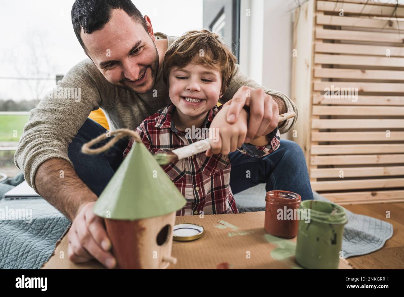Glücklicher Vater und Sohn, die zusammen zu Hause ein Modellhaus malen Stockfoto