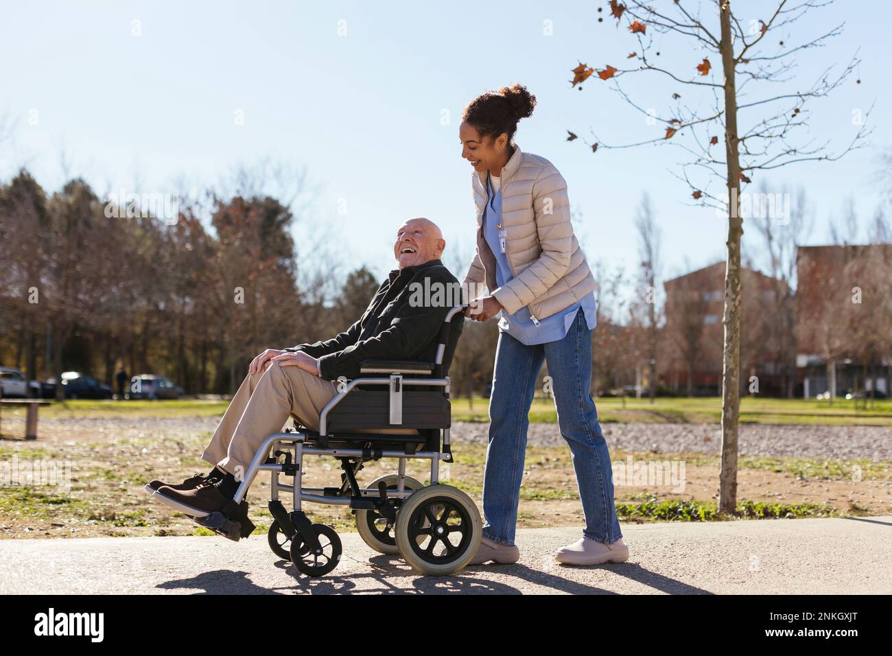 Eine Frau, die einem älteren Mann im Rollstuhl im Park assistiert Stockfoto