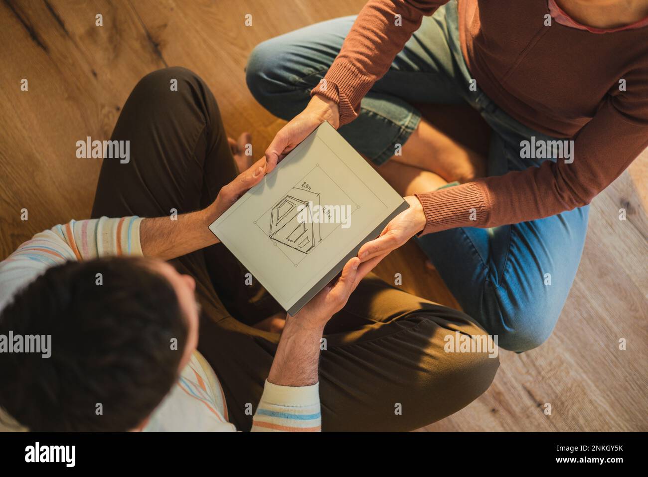 Mann und Frau, die einen Plan von einem Haus haben, das zu Hause mit überkreuzten Beinen sitzt Stockfoto