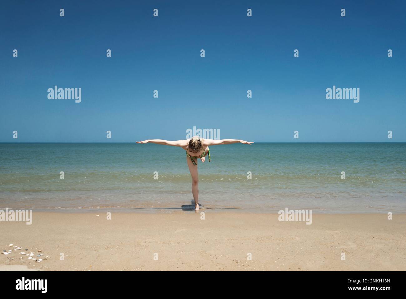 Frau mit ausgestreckten Armen, die am Strand steht Stockfoto