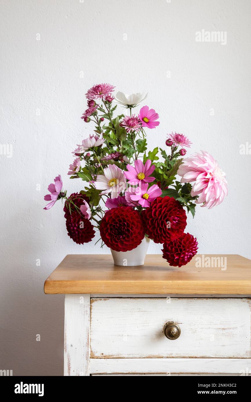 Blumenstrauß aus roten und rosa Herbstblumen auf dem Nachttisch Stockfoto