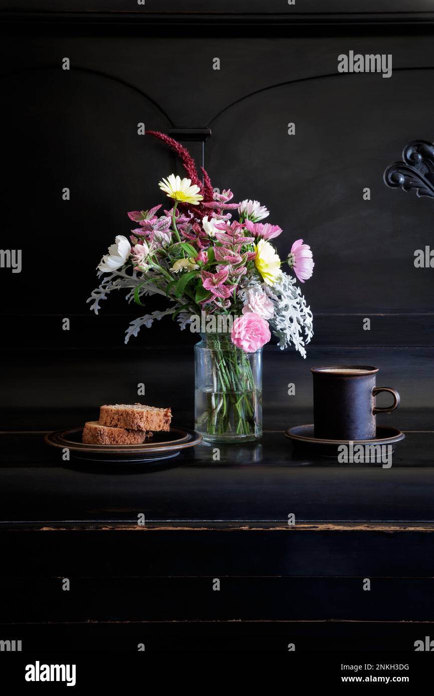 Tasse Kaffee, Kuchenstrauß mit Blumen der Saison auf dem Klavier Stockfoto