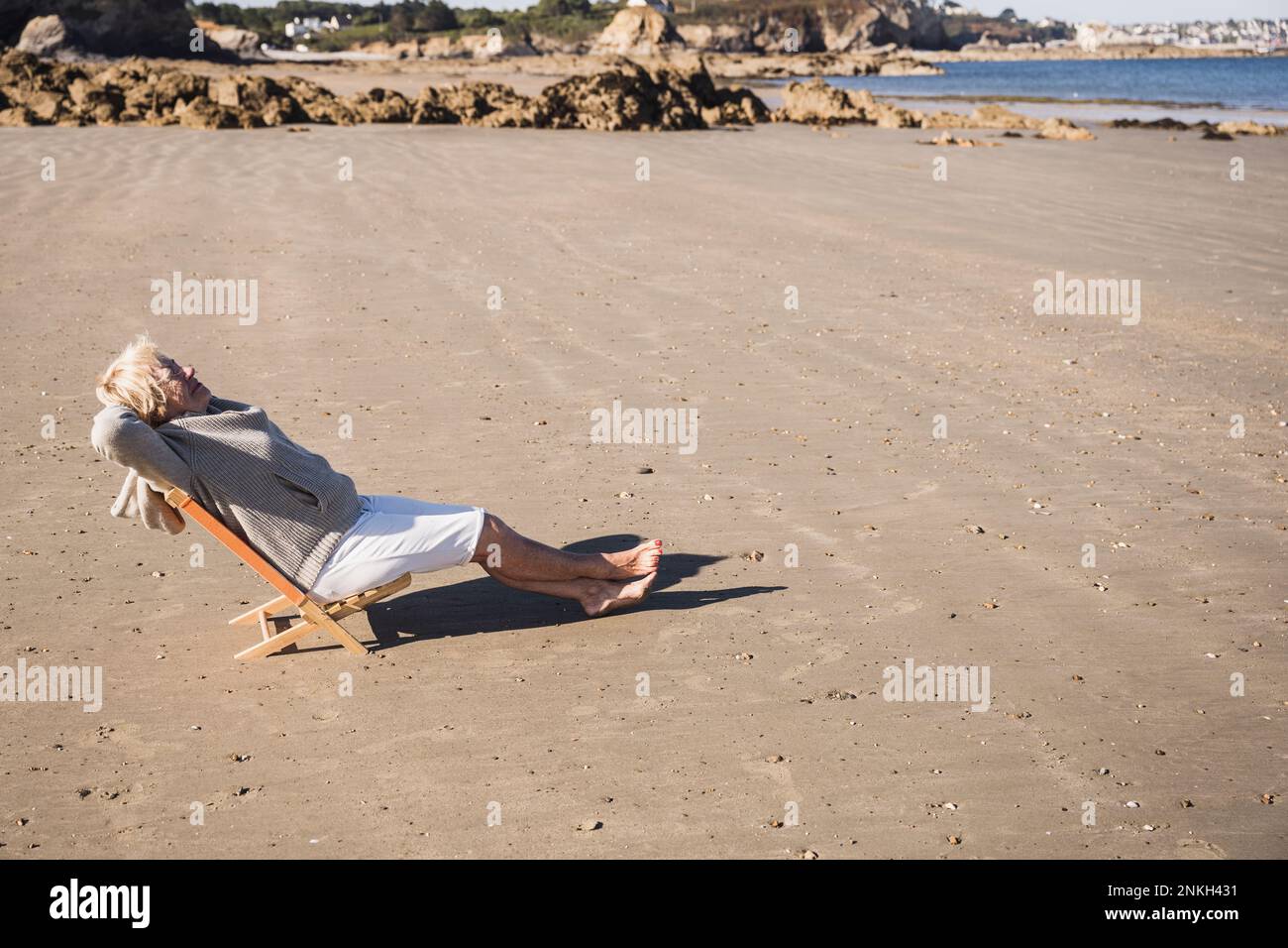 Ältere Frau, die sich am sonnigen Tag am Strand entspannt Stockfoto