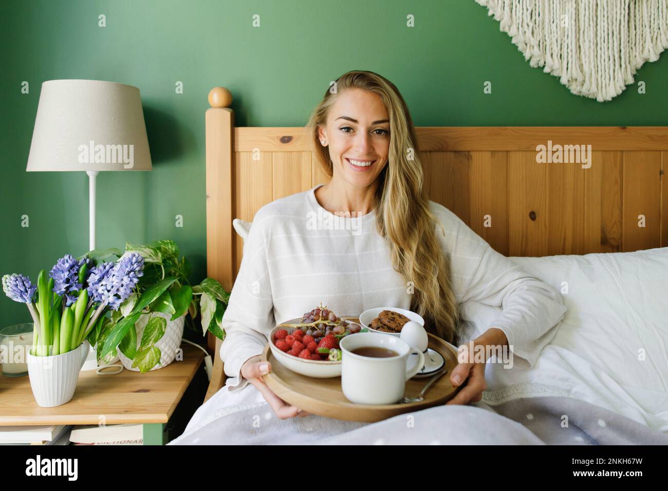 Glückliche Frau, die zu Hause mit Frühstück im Bett sitzt Stockfoto