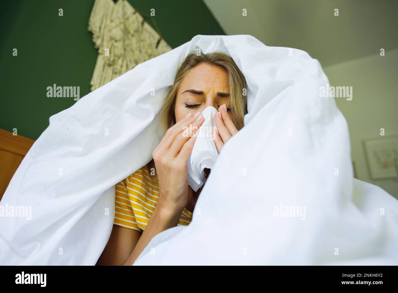 Eine Frau unter einer Decke, die zu Hause im Bett die Nase mit Taschentuch abwischte Stockfoto