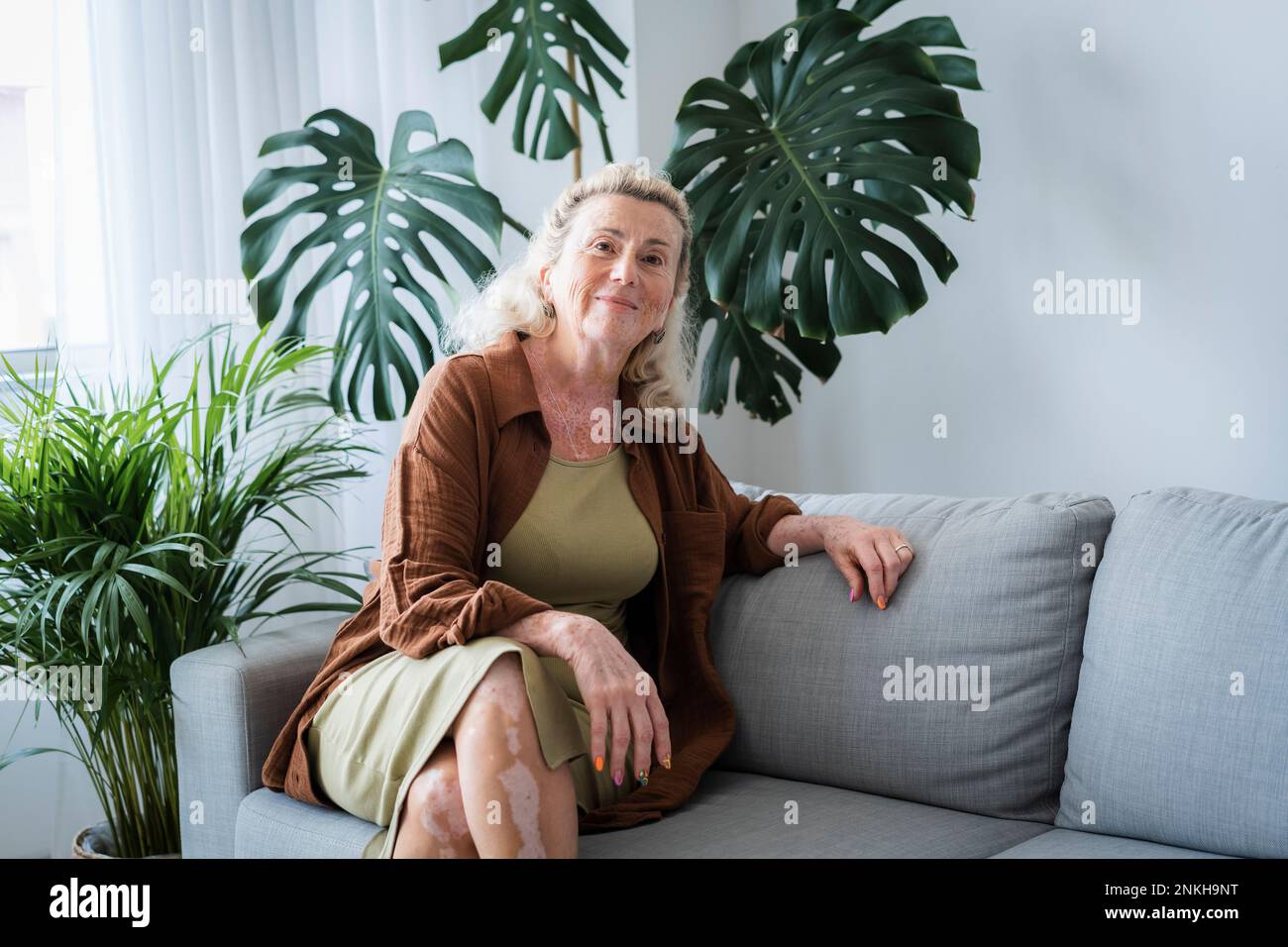 Lächelnde ältere Frau, die zu Hause auf dem Sofa sitzt Stockfoto