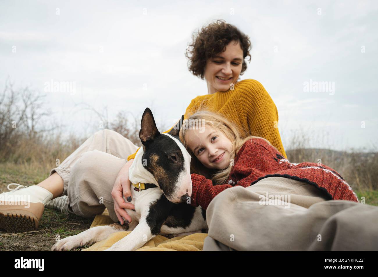 Tochter und Mutter entspannen sich mit Hund vor dem Himmel Stockfoto