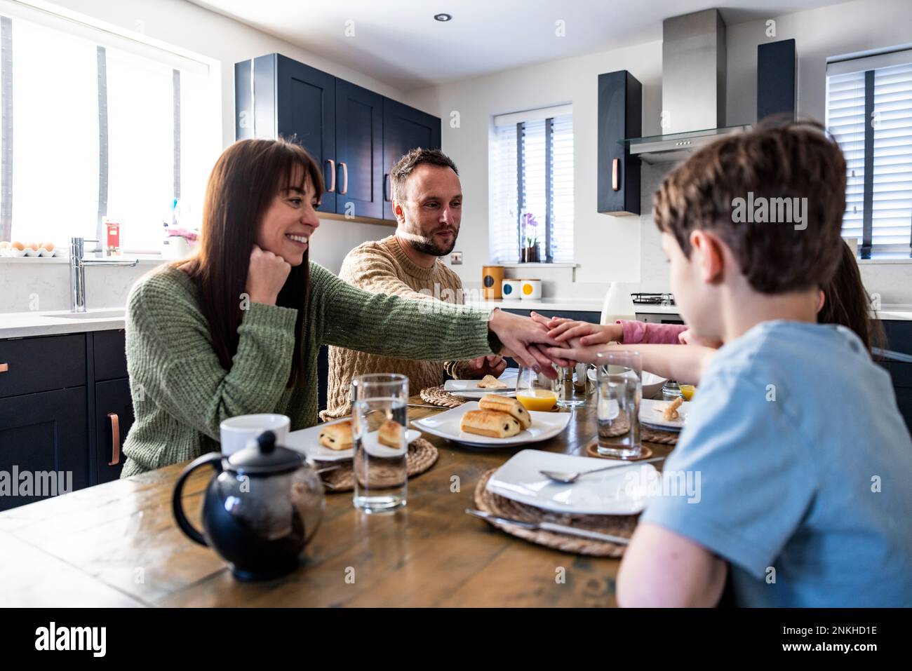 Eine glückliche Familie genießt gemeinsam das Frühstück mit gestapelten Händen am Tisch Stockfoto