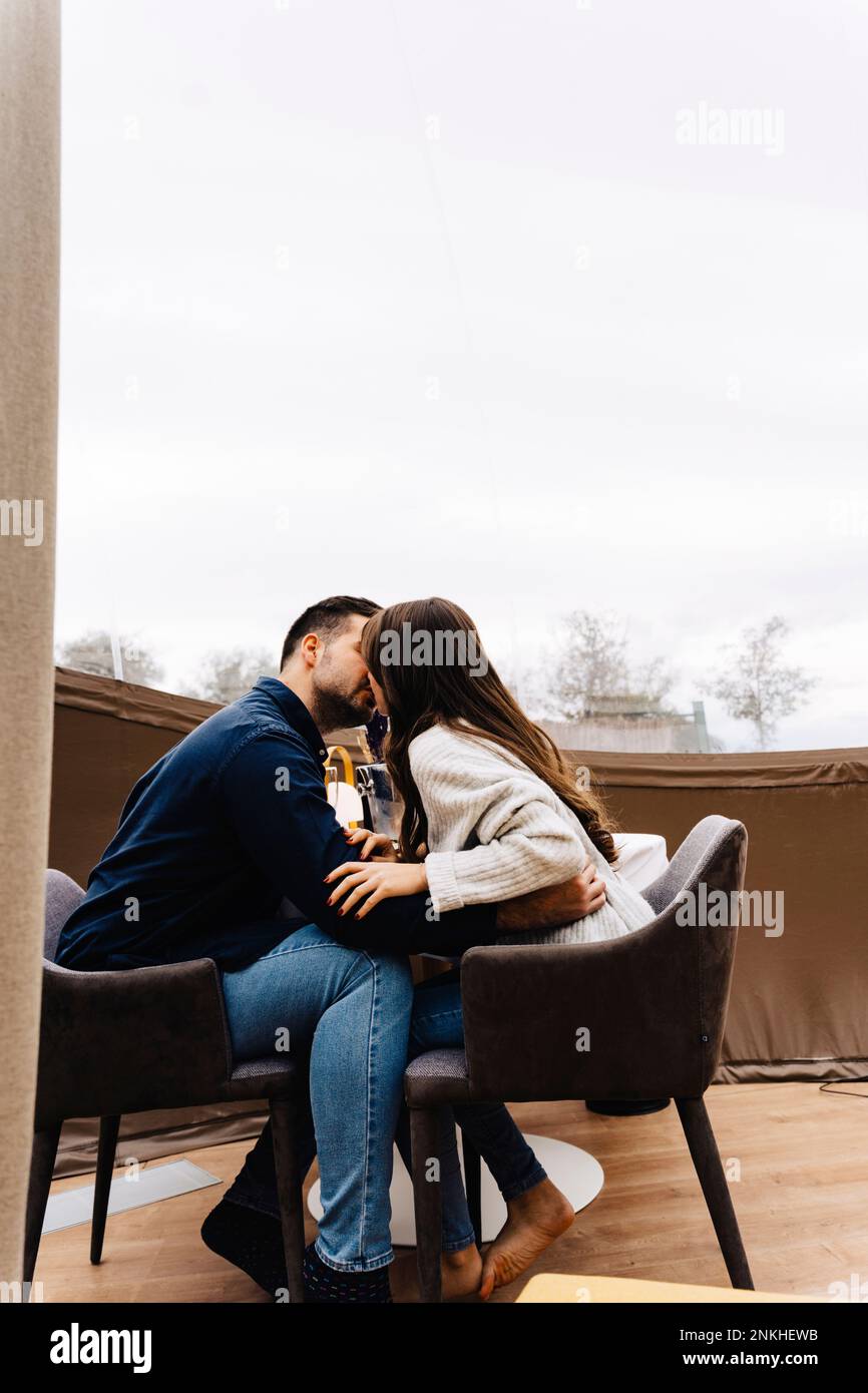 Ein junges Paar sitzt auf einem Stuhl und küsst sich im Kuppelzelt-Hotel Stockfoto