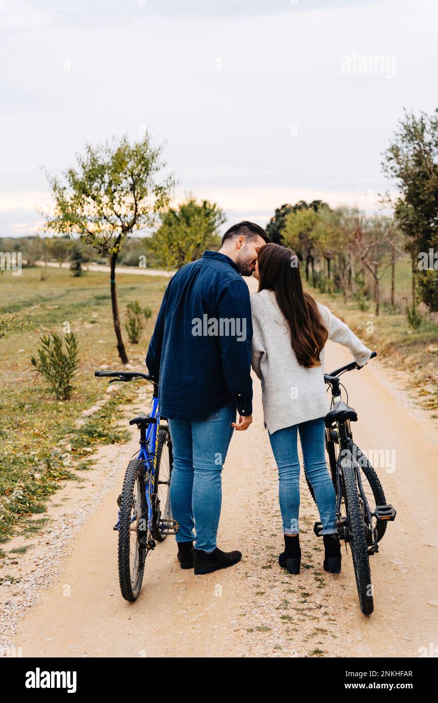 Ein junges Paar mit Fahrrädern, das sich auf einer unbefestigten Straße küsst Stockfoto