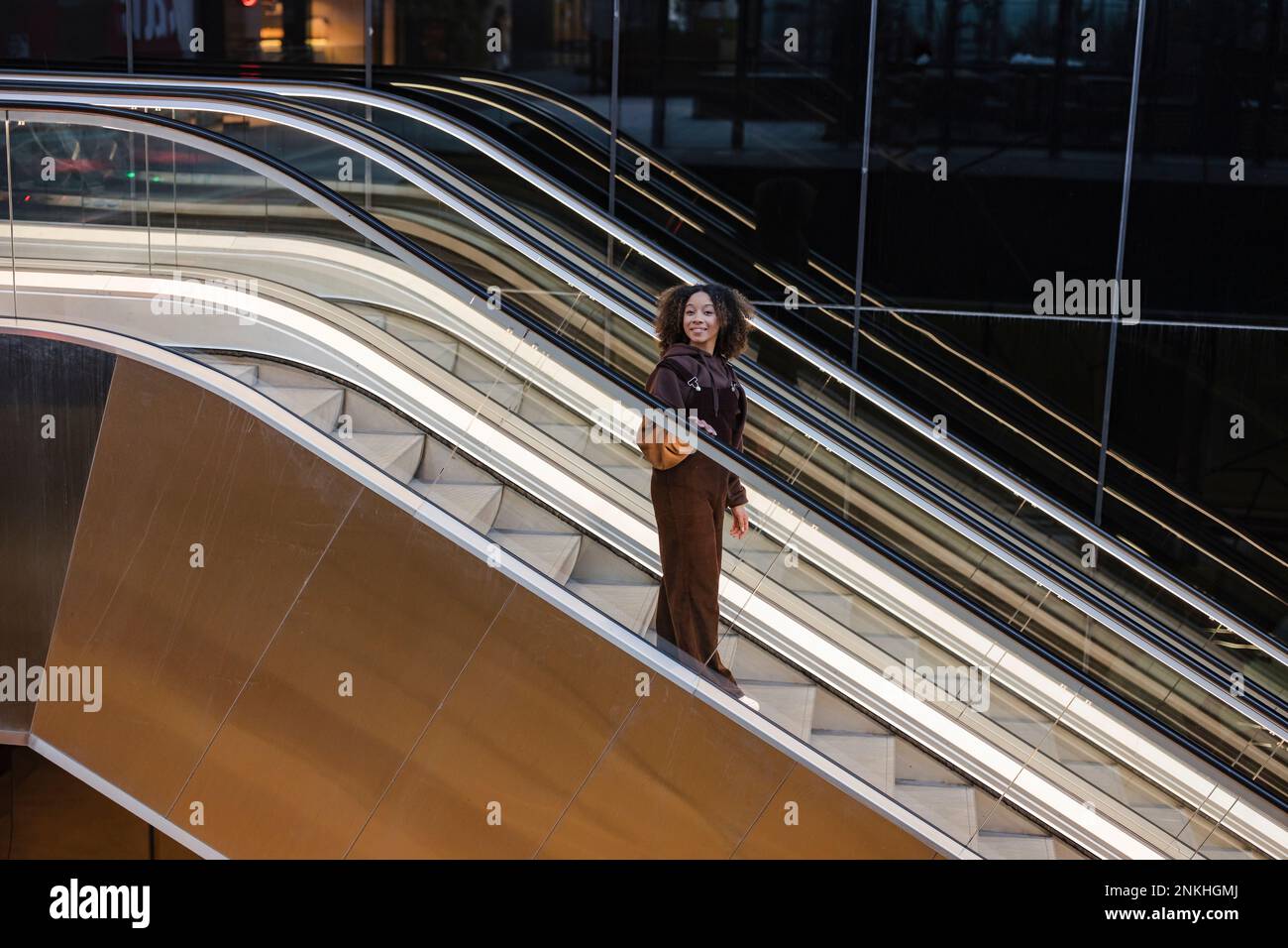 Lächelnde junge Frau, die die Rolltreppe hinunterfährt Stockfoto