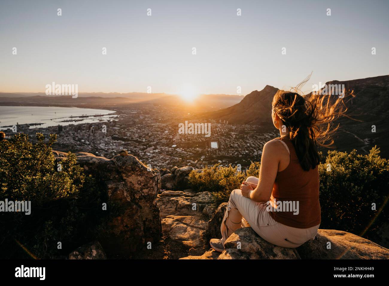 Eine Frau auf dem Felsen, die bei Sonnenaufgang die Stadtlandschaft vom Lion's Head Mountain aus betrachtet Stockfoto