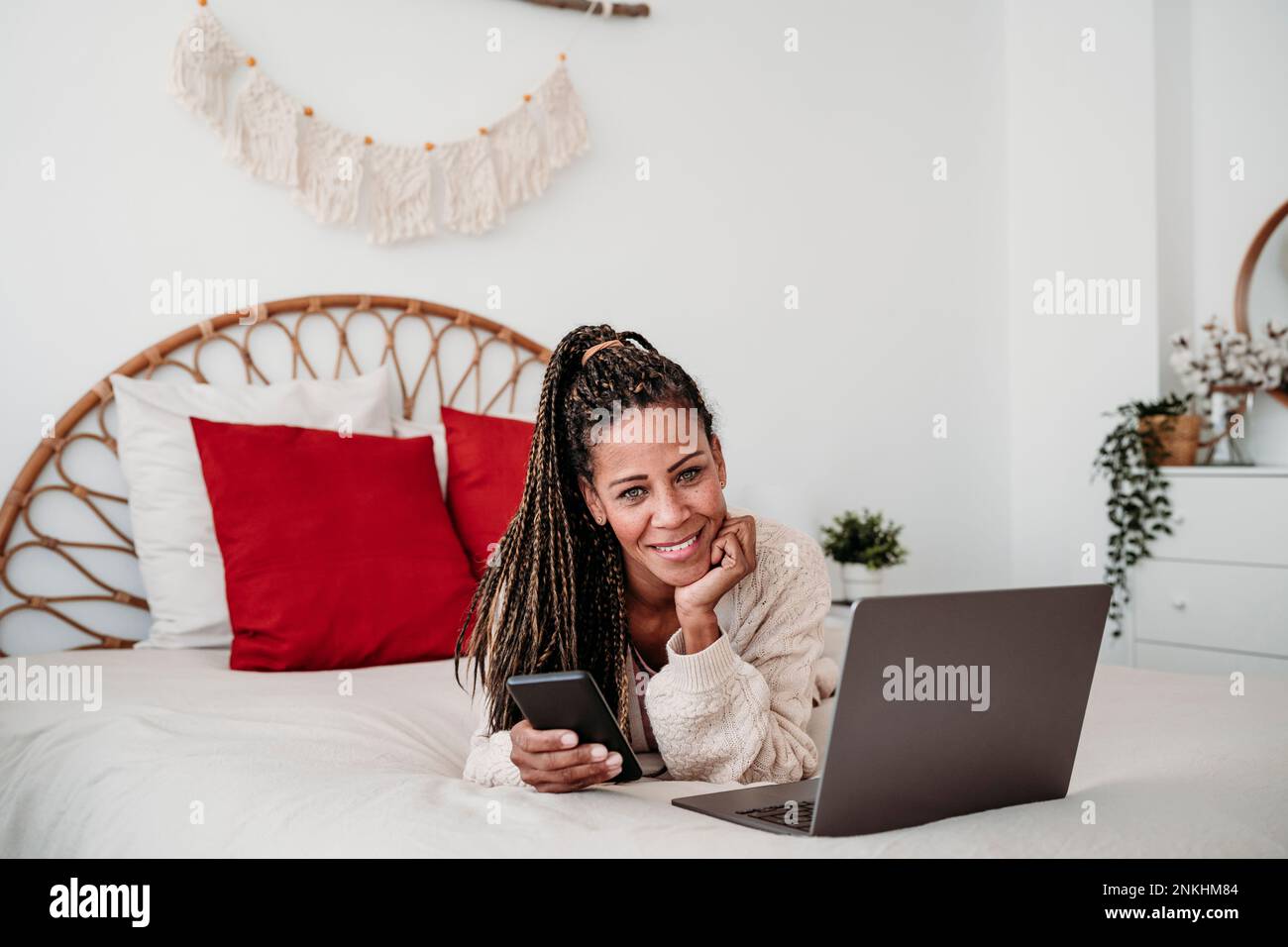 Lächelnder Freiberufler, der zu Hause mit Laptop und Smartphone im Bett liegt Stockfoto