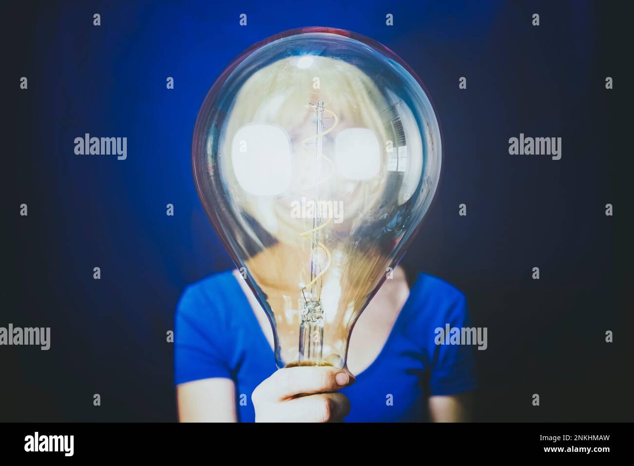 Frau, die eine große, beleuchtete Glühlampe vor blauem Hintergrund hält Stockfoto