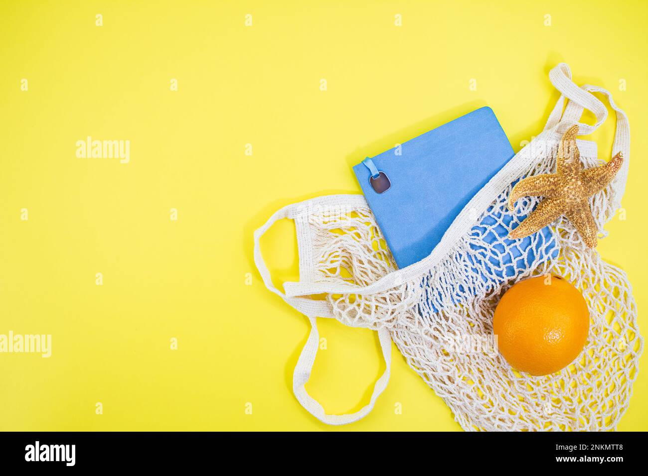 Notizbuch mit Seesternen und Orange mit Tasche mit Schnur auf gelbem Hintergrund. Konzept von Urlaub, Reisen, Sommer in heißen Ländern. Speicherplatz kopieren Stockfoto