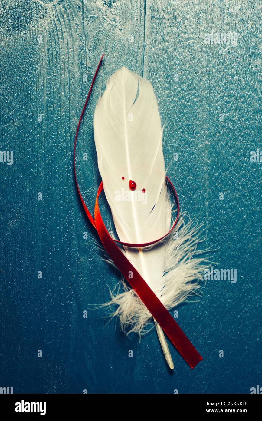 Weiße Feder mit Blutstropfen und rotem Band Stockfoto