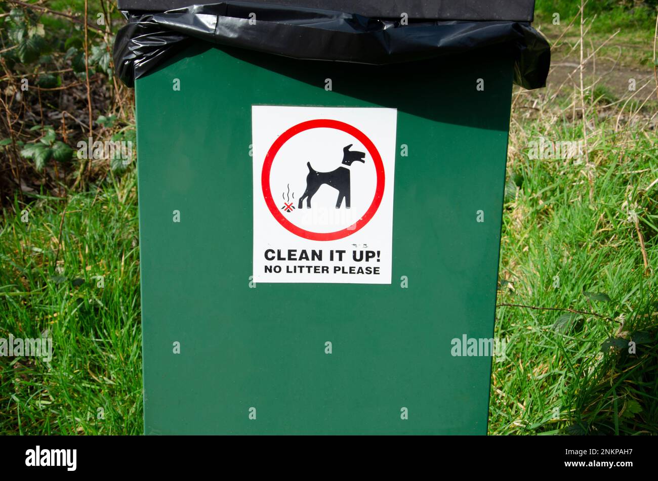 Schild „Clean up after your dog“ auf einem Abfalleimer für Hundekacke mit weißem Hintergrund und schwarzer und roter Schrift Stockfoto