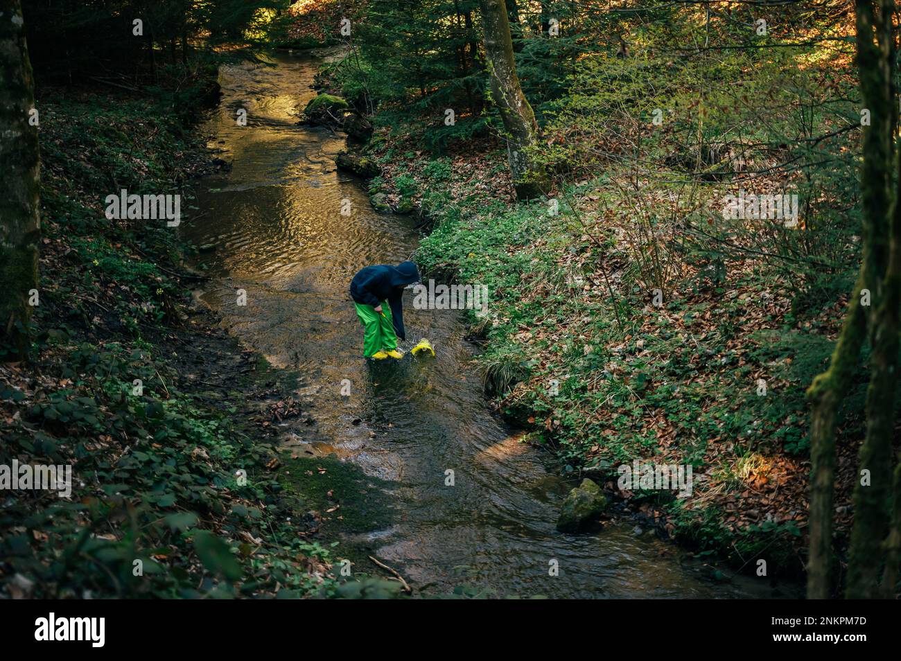 Person im Wald. Asiatische Kinderangeln mit einem Netz, um die Natur zu entdecken. Ein Junge in Blau spielt im Frühling in einem Bach. Stockfoto