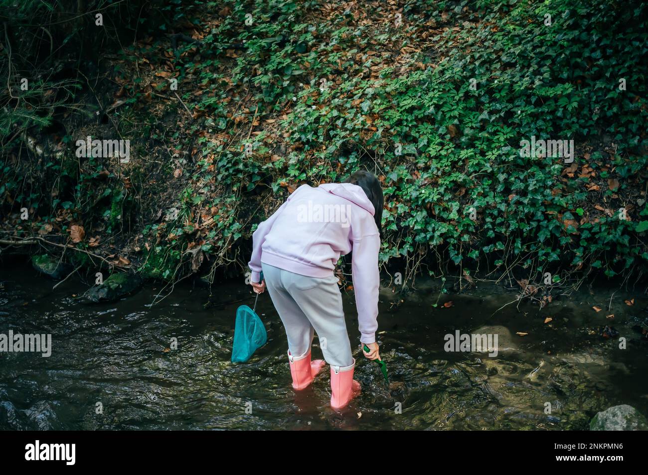 Person im Wald. Asiatische Kinderangeln mit einem Netz, um die Natur zu entdecken. Ein Mädchen in Pink spielt im Frühling in einem Bach. Stockfoto