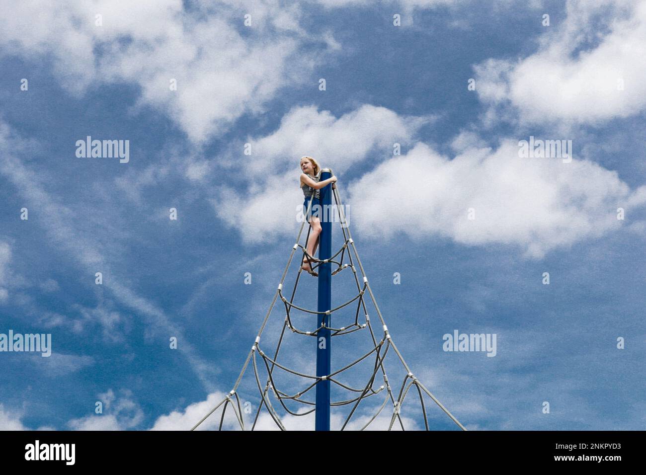 Ein Mädchen oben am Seil klettert mit Wolken gegen den Himmel Stockfoto
