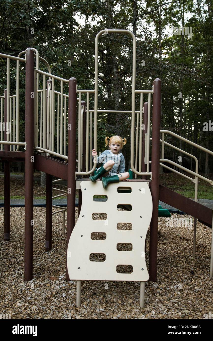 Ein junges Mädchen, das auf einem Klettergerät im Spielpark sitzt Stockfoto