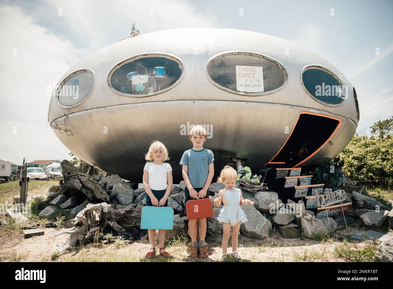Drei Kinder stehen vor einem fremden Raumschiff und halten Koffer Stockfoto