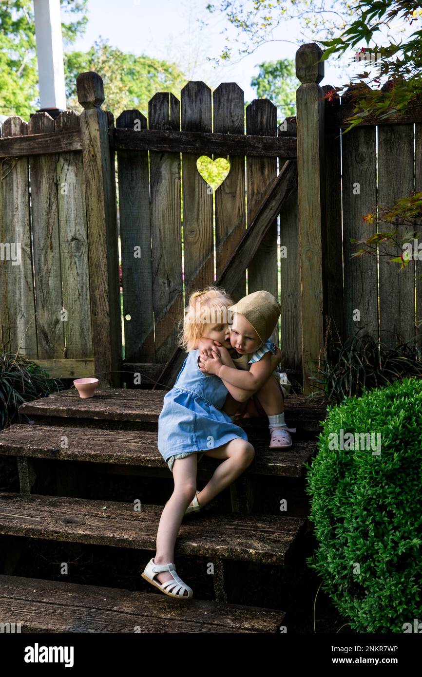 Zwei Mädchen, die sich auf Holztreppen im Garten umarmen Stockfoto