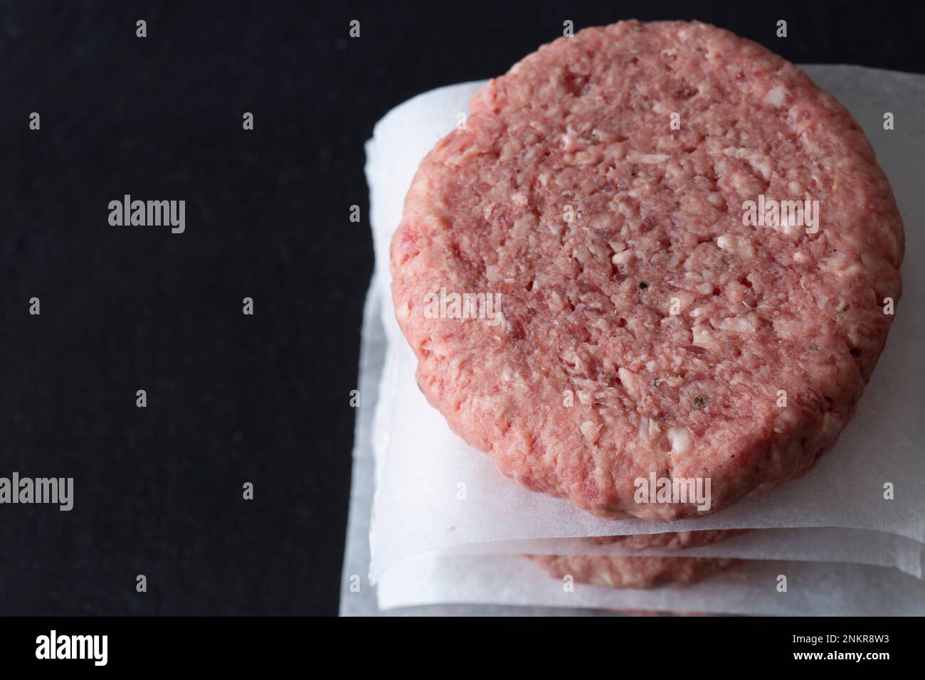 Rohe Rindfleischburger, die auf einem Schieferschneidbrett gestapelt und mit fettfestem Papier getrennt sind Stockfoto