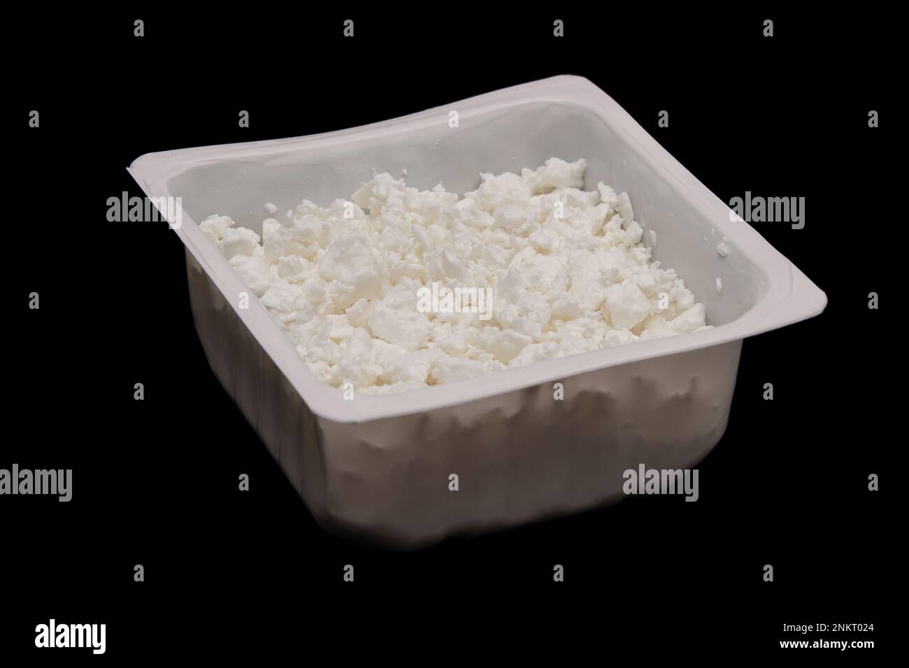 Hüttenkäse in einem Behälter, isoliert auf schwarzem Hintergrund. Quark nach europäischer Art. Seitenansicht Stockfoto