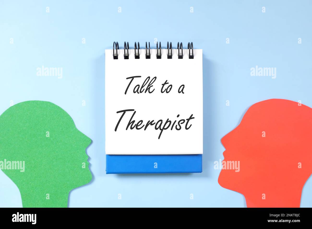 Gespräch mit einem Therapeuten, Psychotherapie und Beratung für ein psychisches Gesundheitskonzept. Flache Laienzusammensetzung des menschlichen Kopfprofils mit blauem Notizblock. Stockfoto