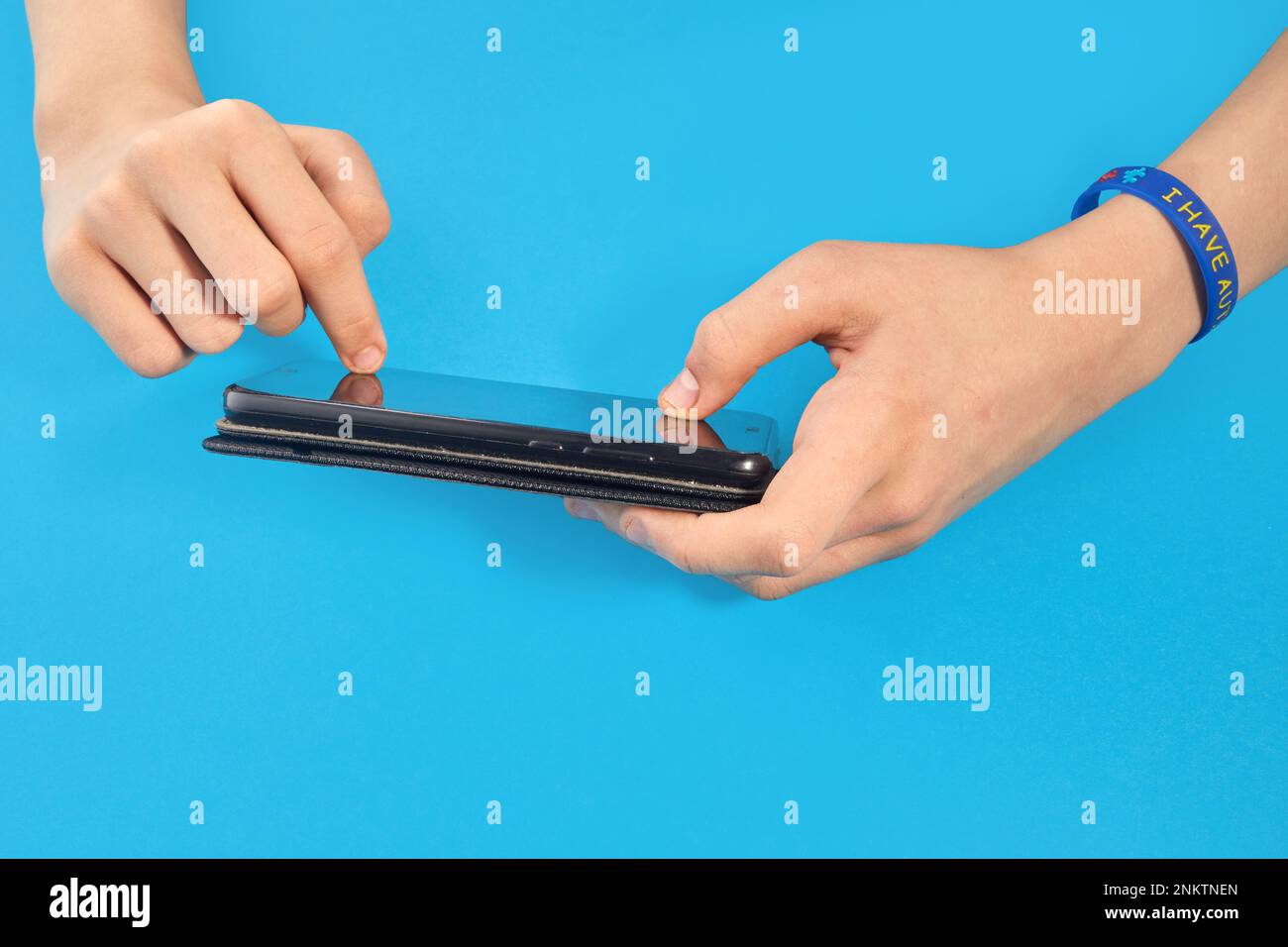 Ein autistischer Junge, der das Telefon in zwei Händen hält. Autismusbewusstsein. Stockfoto