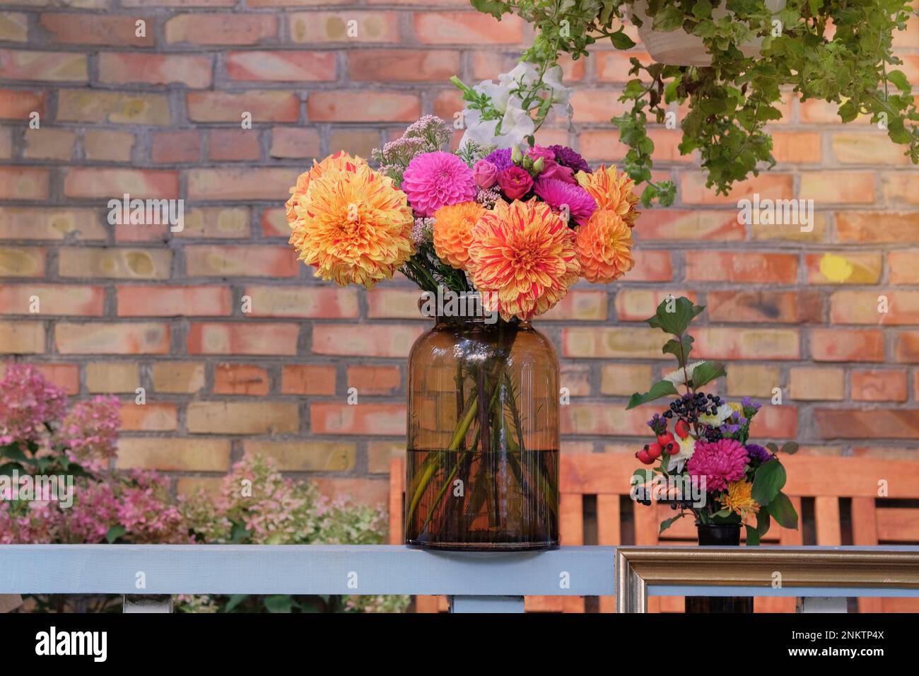 Blumendesign. Rosen, Aster, Dahlien in Glasvase im Garten vor einer Ziegelmauer. Sonniger Tag. Stockfoto