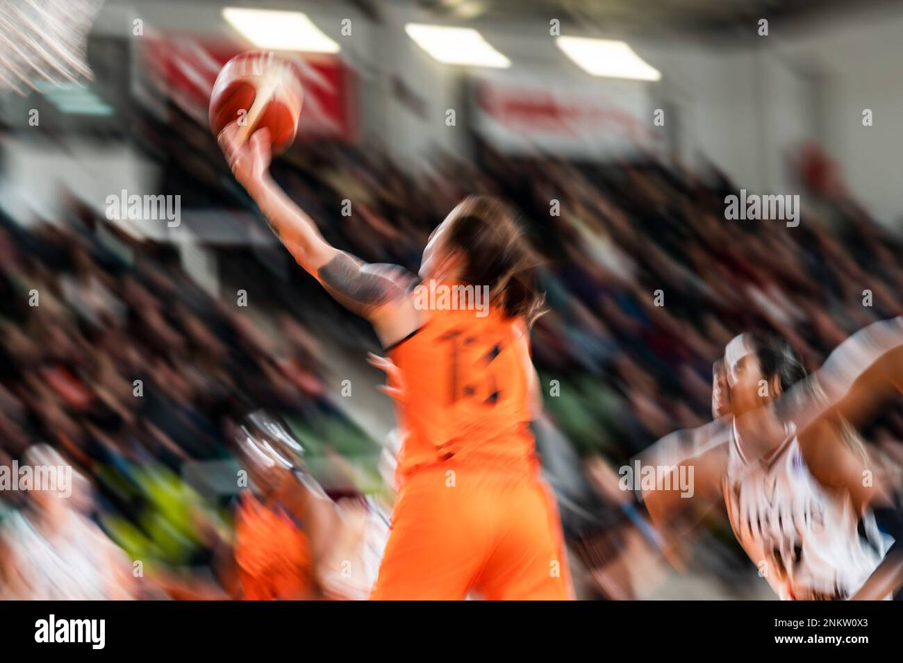 Eine Spielerin wirft den Ball während des Basketballspiels in den Korb. Absichtliches blaues Bild (Tätowierung auf dem Arm zusätzlich verschmiert) Stockfoto