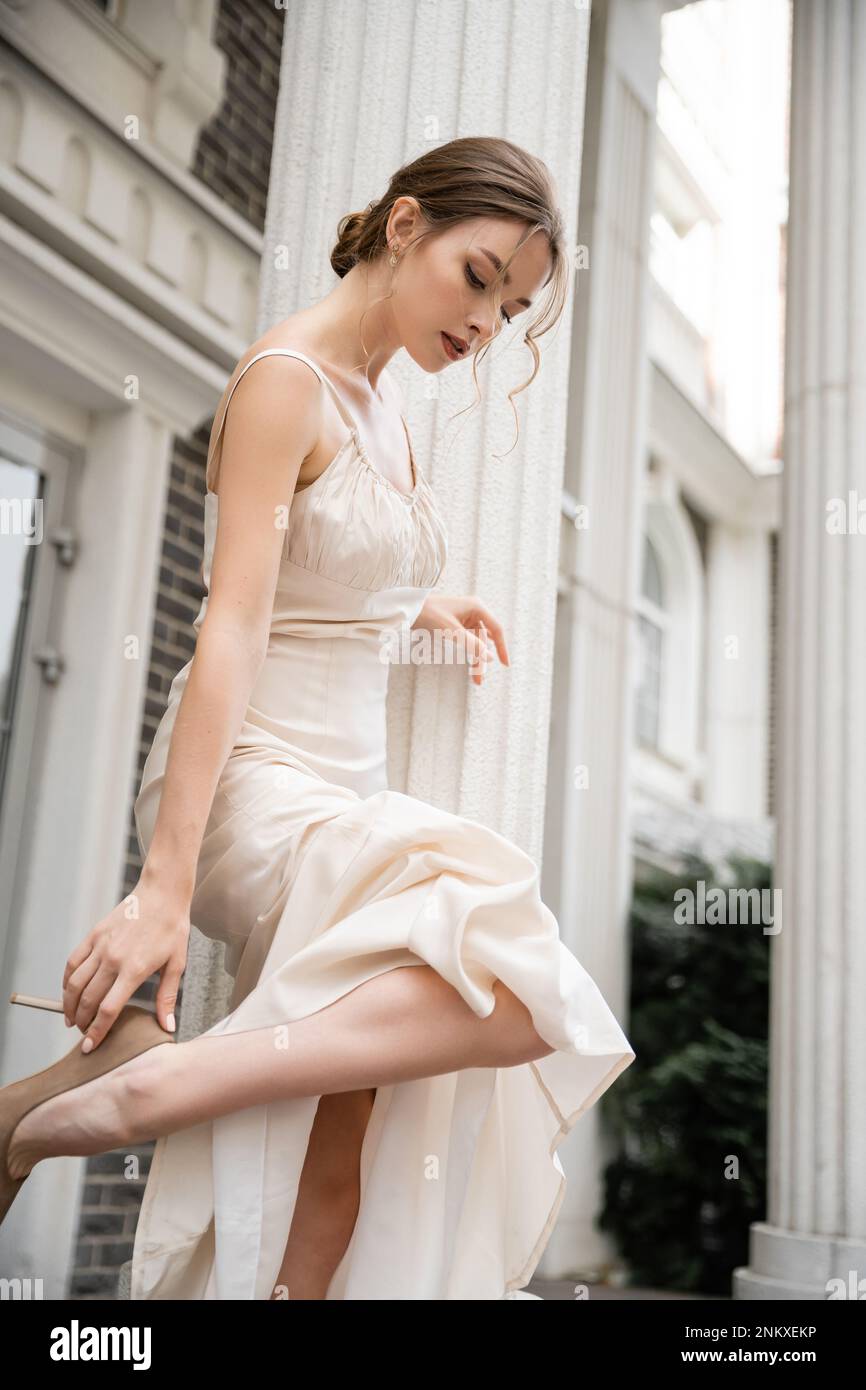 Junge Braut in Hochzeitskleid in Schuhen mit hohen Absätzen in der Nähe des Hauses, Stock Image Stockfoto