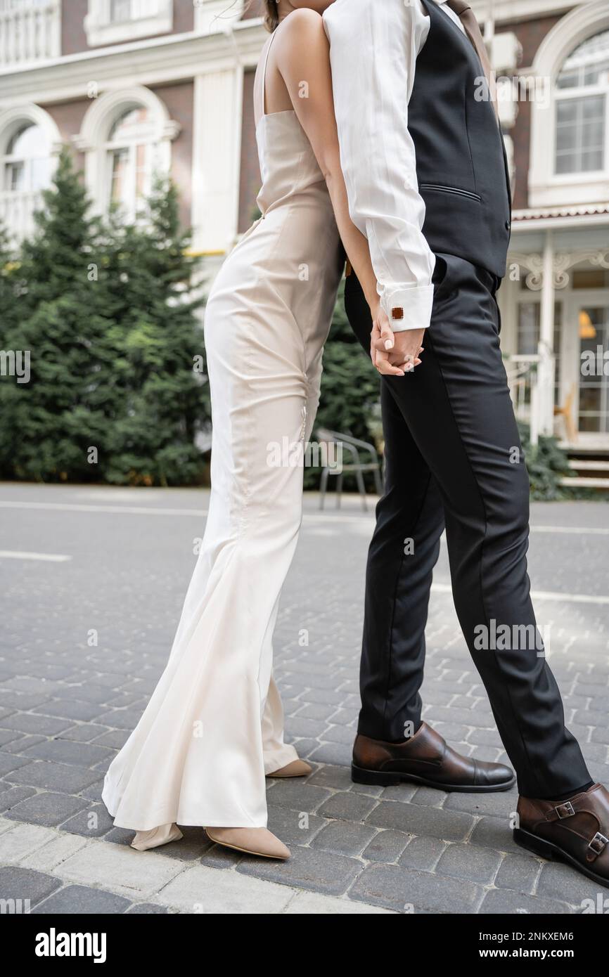 Kurzer Blick auf junge Braut und Bräutigam im Hochzeitskleid und Anzug, die sich draußen die Hände halten, Stockbild Stockfoto