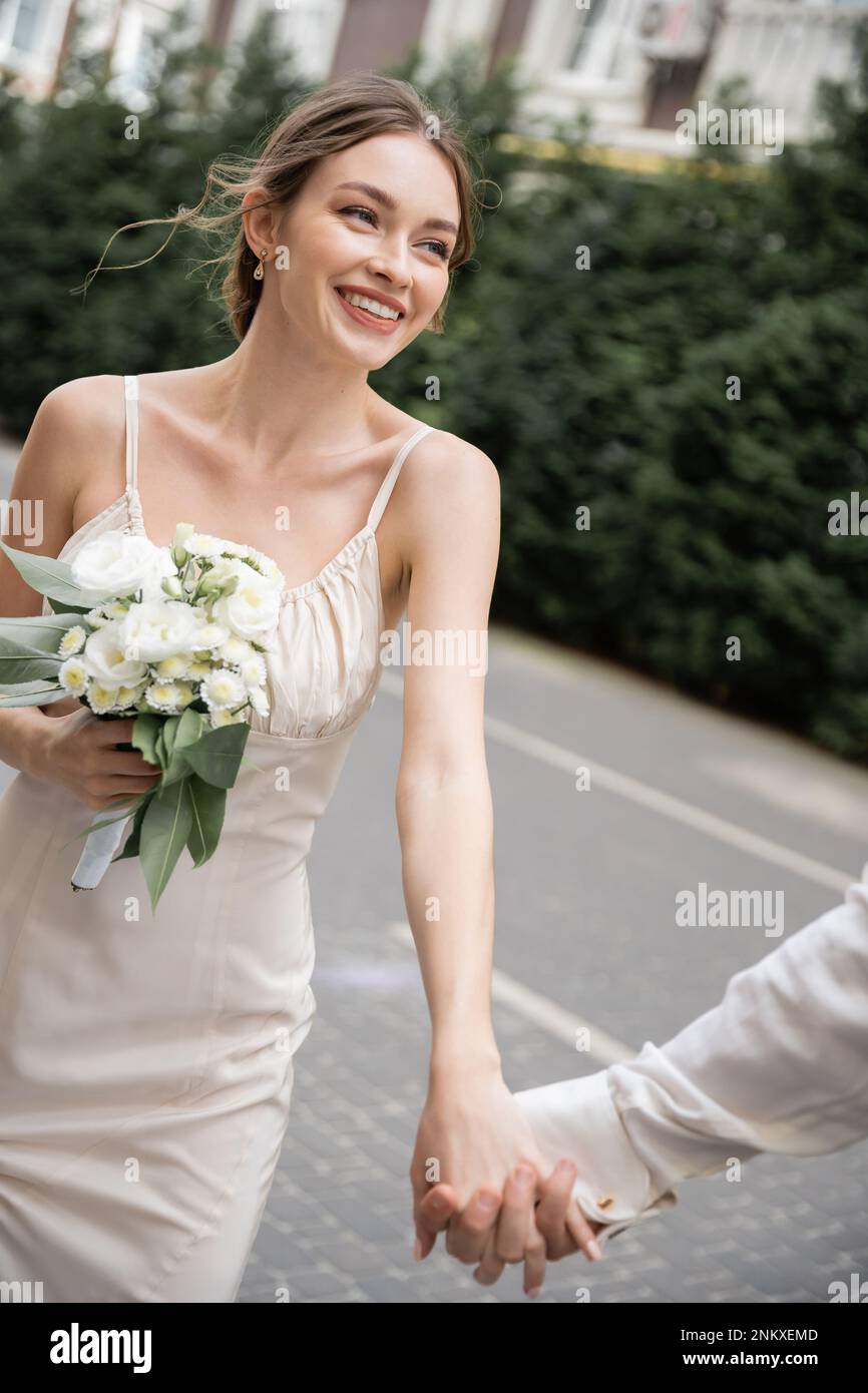 Bräutigam hält Hand der glücklichen Braut in weißem Kleid mit Hochzeitsstrauß, Stockbild Stockfoto