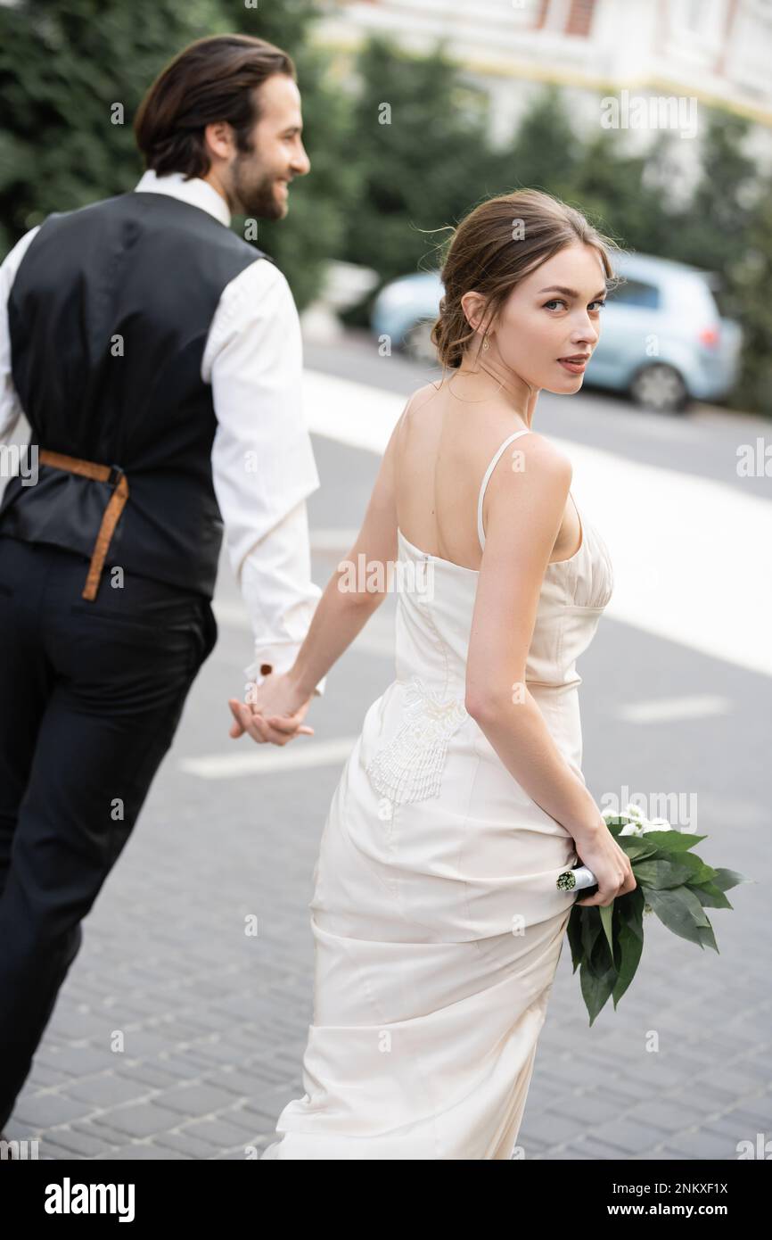 Der Bräutigam hält die Hand einer wunderschönen Braut in einem Hochzeitskleid mit Blumenstrauß, Stockbild Stockfoto