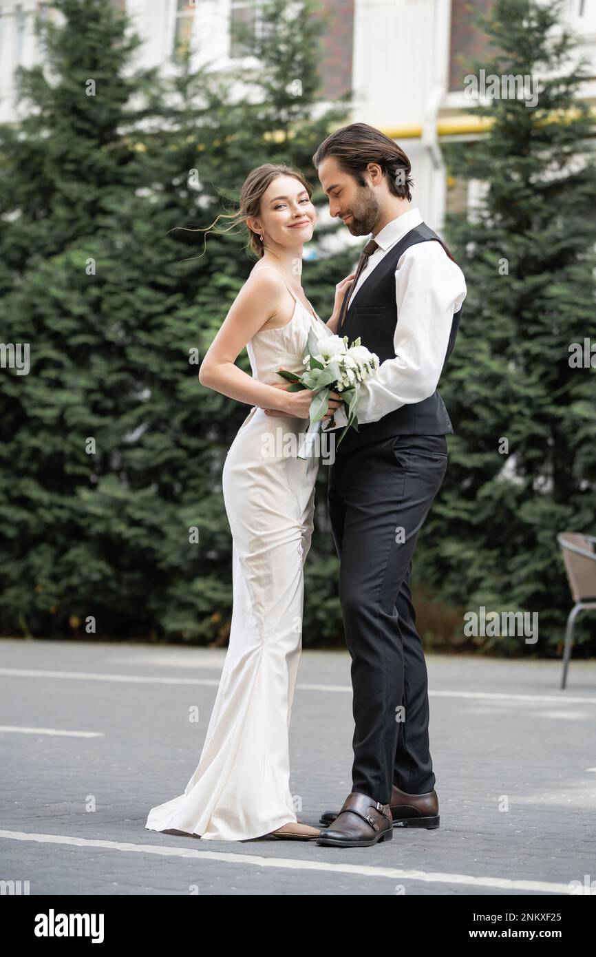 Bärtige Bräutigam in Weste mit fröhlicher Braut in weißem Kleid und  Hochzeitsstrauß, Stockbild Stockfotografie - Alamy