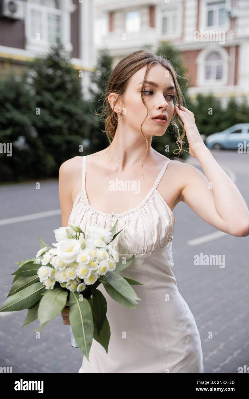 Junge Frau in Hochzeitskleid mit Blumenstrauß und wegblickend, Stockbild Stockfoto