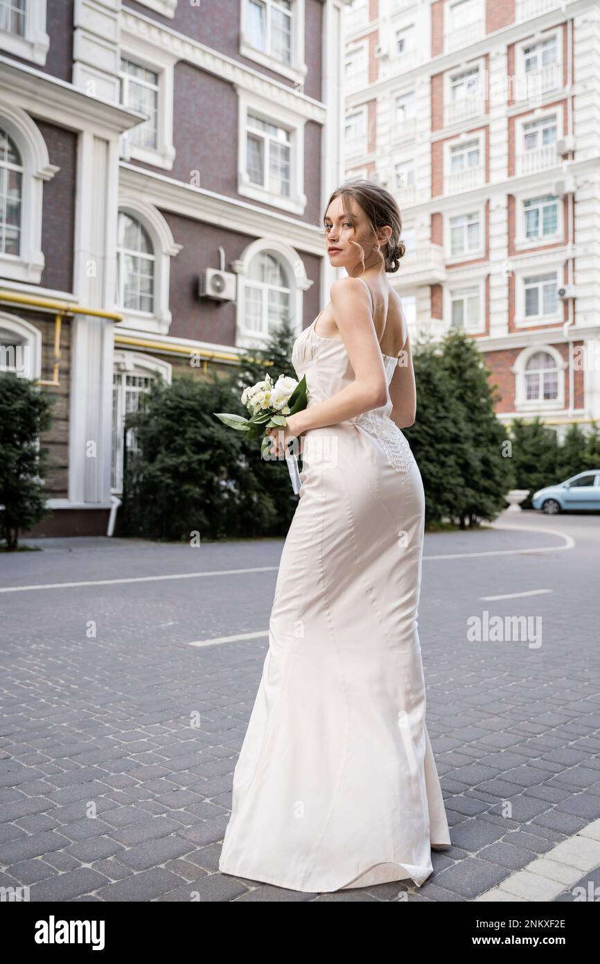 Blick über die gesamte Länge einer jungen Frau in weißem Kleid mit Hochzeitsstrauß, Stockbild Stockfoto