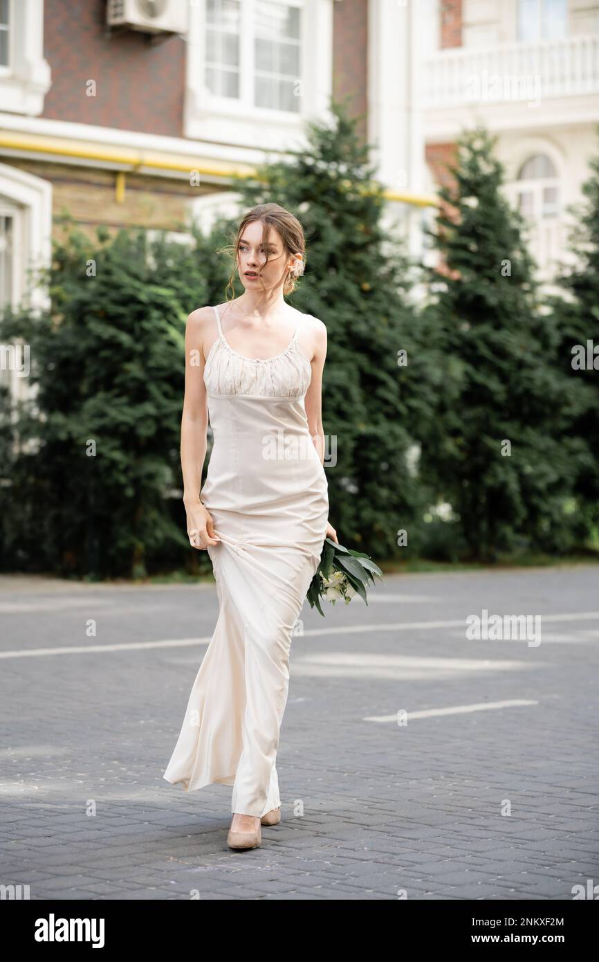 Lange Braut in weißem Kleid mit Hochzeitsstrauß und Spaziergängen auf der Straße, Bild der Börse Stockfoto