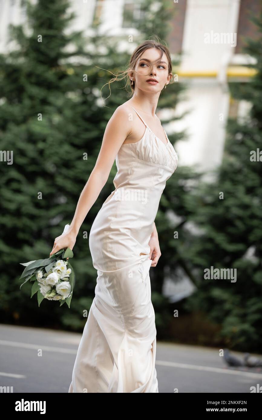 Hübsche Frau in weißem Kleid mit Hochzeitsstrauß mit blühenden Blumen, Stockbild Stockfoto