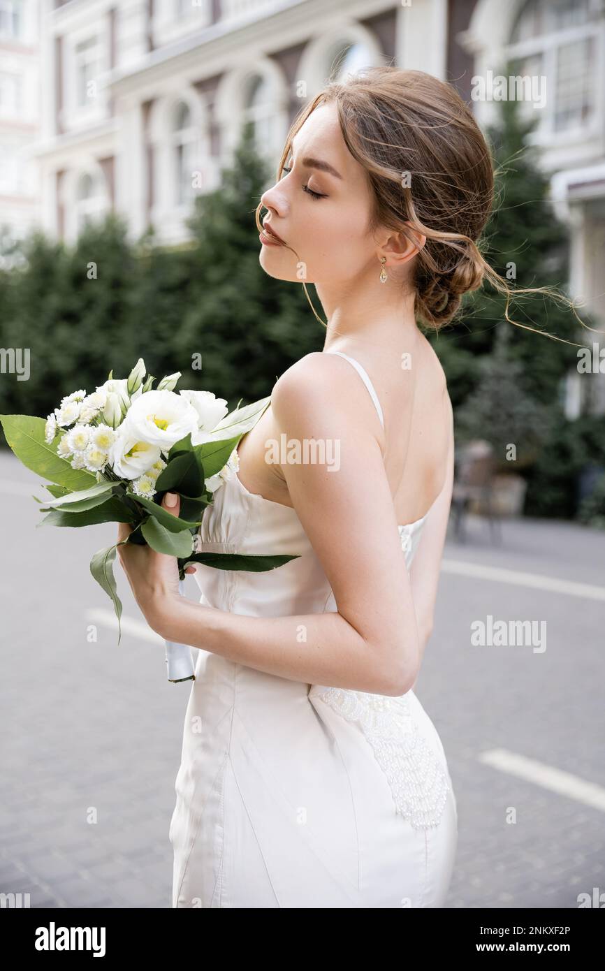 Junge Braut in weißem Kleid mit geschlossenen Augen und Hochzeitsstrauß, Stockbild Stockfoto