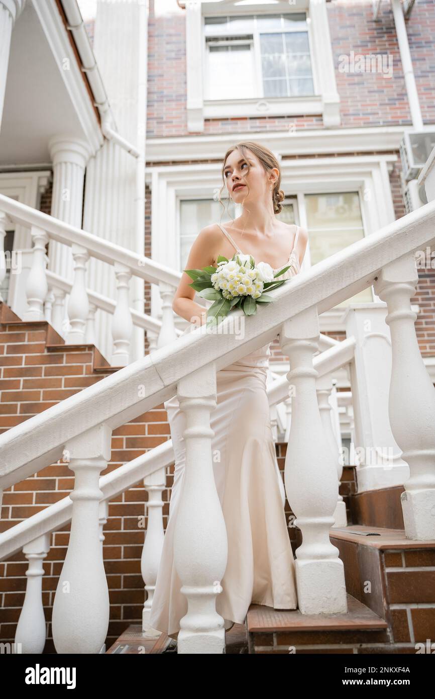 Braut im Hochzeitskleid, mit Strauß und Blick in die Nähe des Hauses, Stockbild Stockfoto
