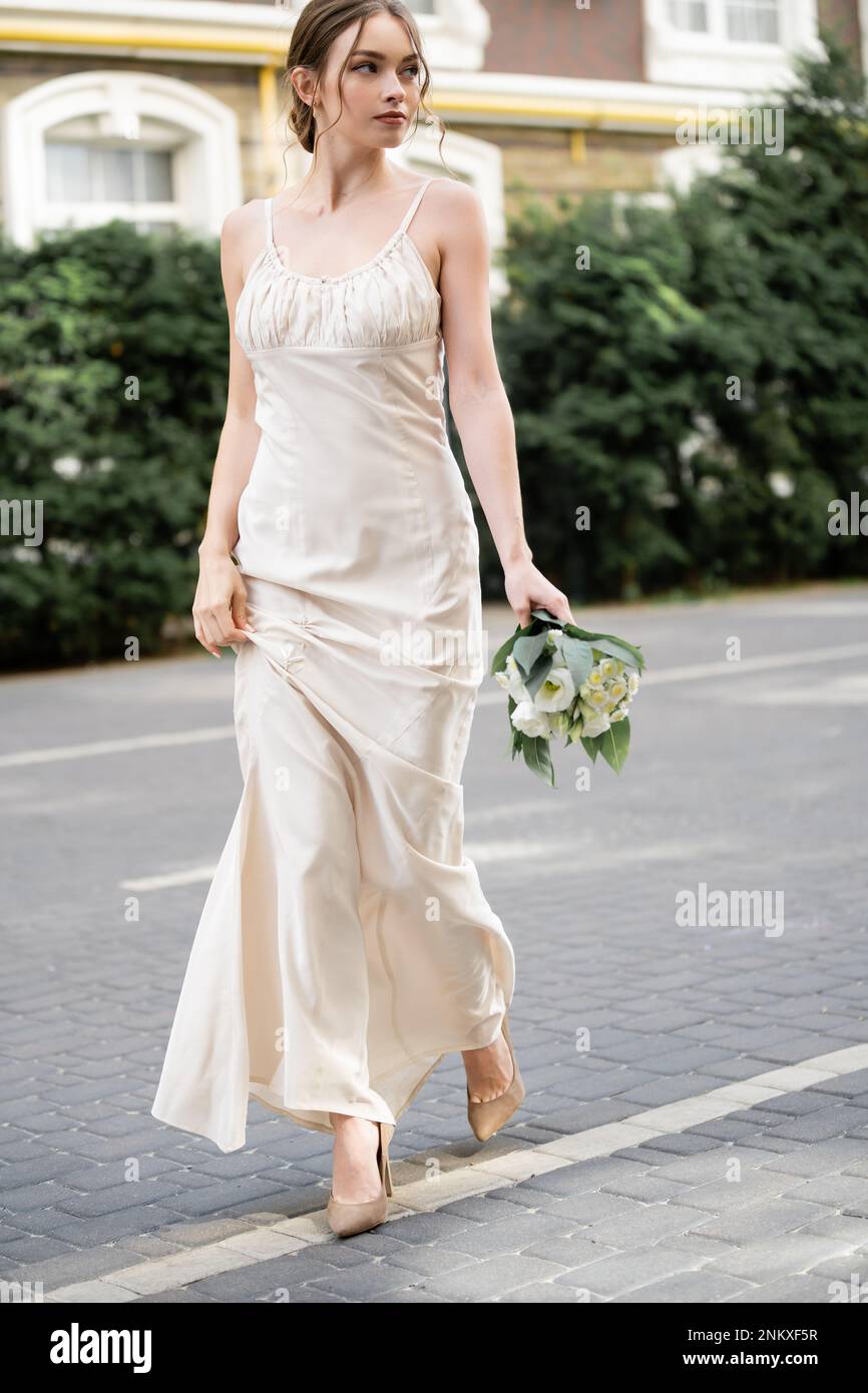 Lange junge Braut in weißem Kleid mit Hochzeitsstrauß mit Blumen, Stockbild Stockfoto