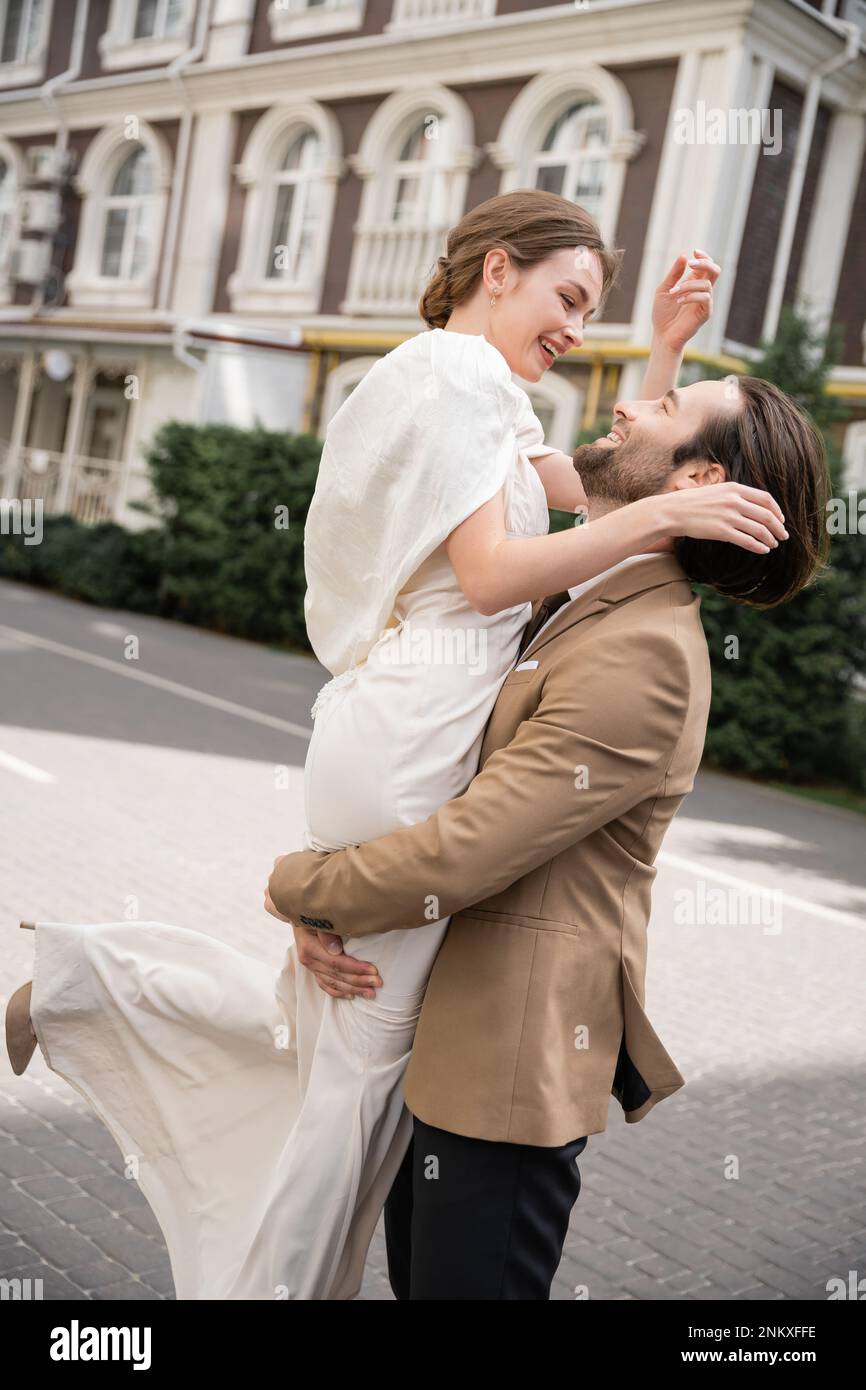 Bärtiger Bräutigam in formeller Kleidung, die fröhliche Braut in weißem Kleid draußen, Stock Image Stockfoto